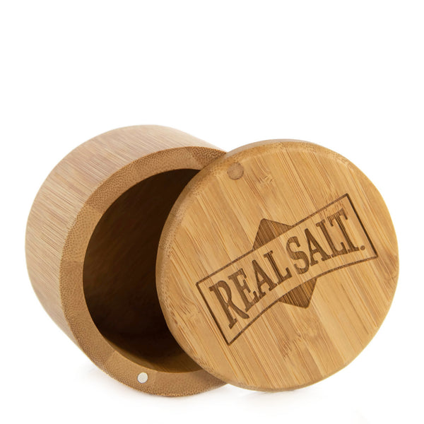 Open bamboo salt cellar with the lid beside it, revealing the "Real Salt" inscription engraved on the wood. 
