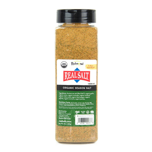A clear jar displays Redmond Real Salt Organic Season Salt, showcasing its blend of spices and ancient sea salt. 
