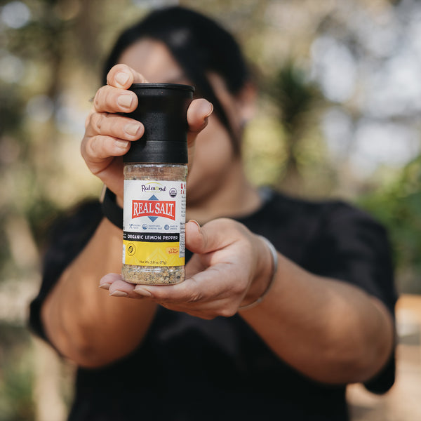A person holds out a grinder of Redmond Real Salt brand organic lemon pepper.