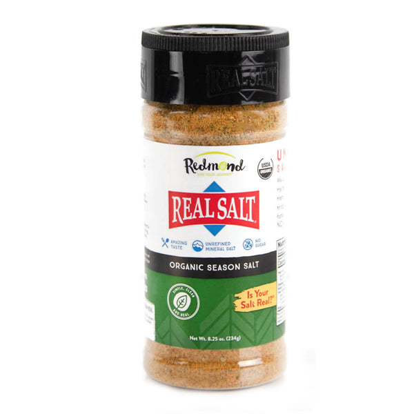 A clear shaker displays Redmond Real Salt's organic season salt, showcasing its natural brown color and coarse grind.