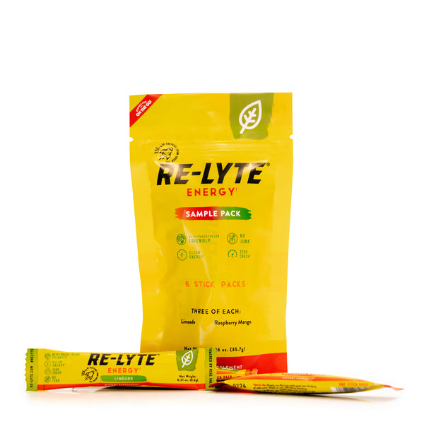 A bright yellow RE-LYTE ENERGY sample pack stands upright with a single-serving stick pack of limeade flavor resting on the surface in front. 
