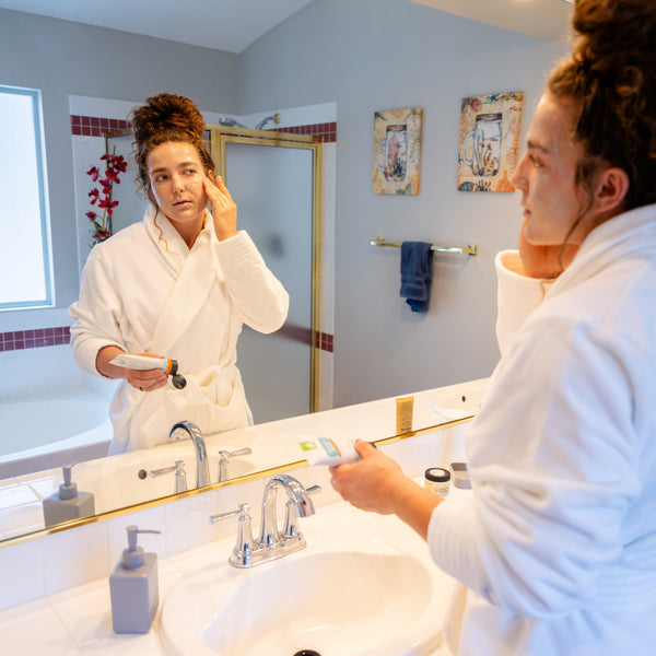 A person applies Redmond Clay Facial Mud with Silver to their face in a bathroom mirror.